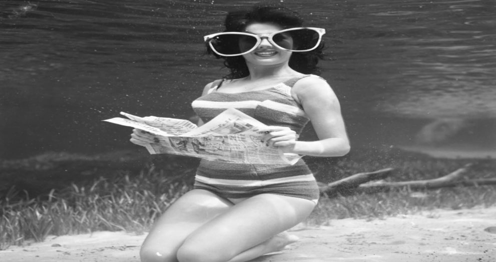 Pat McLauchlin reads a newspaper underwater at Silver Springs, Florida, wearing oversized sunglasses