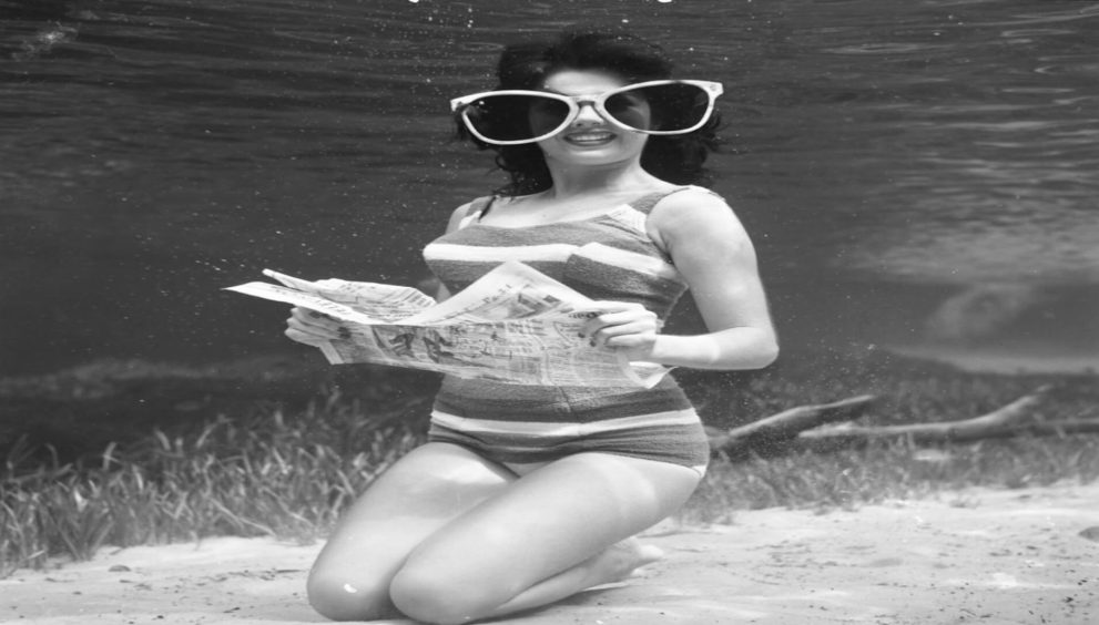Pat McLauchlin reads a newspaper underwater at Silver Springs, Florida, wearing oversized sunglasses