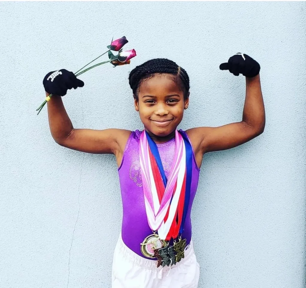Photo of 9-year-old T’yonna Major wearing gymnastics medals and raising her arms in a victory pose.