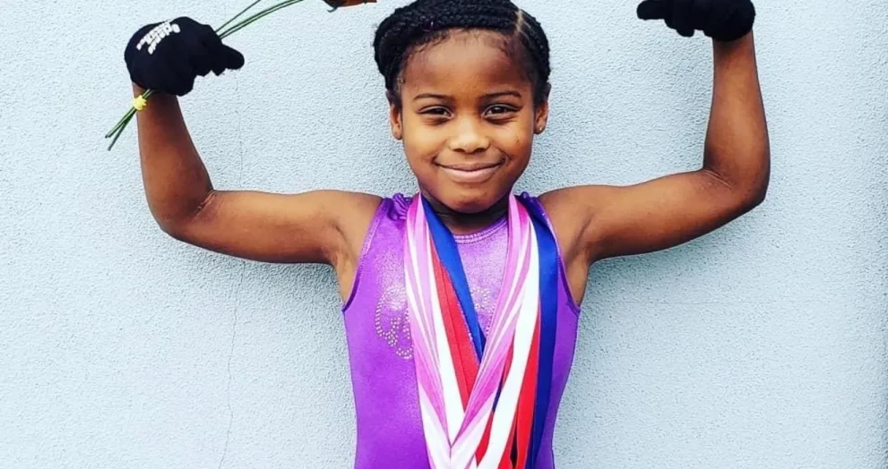 Photo of 9-year-old T’yonna Major wearing gymnastics medals and raising her arms in a victory pose.