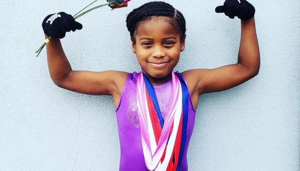Photo of 9-year-old T’yonna Major wearing gymnastics medals and raising her arms in a victory pose.