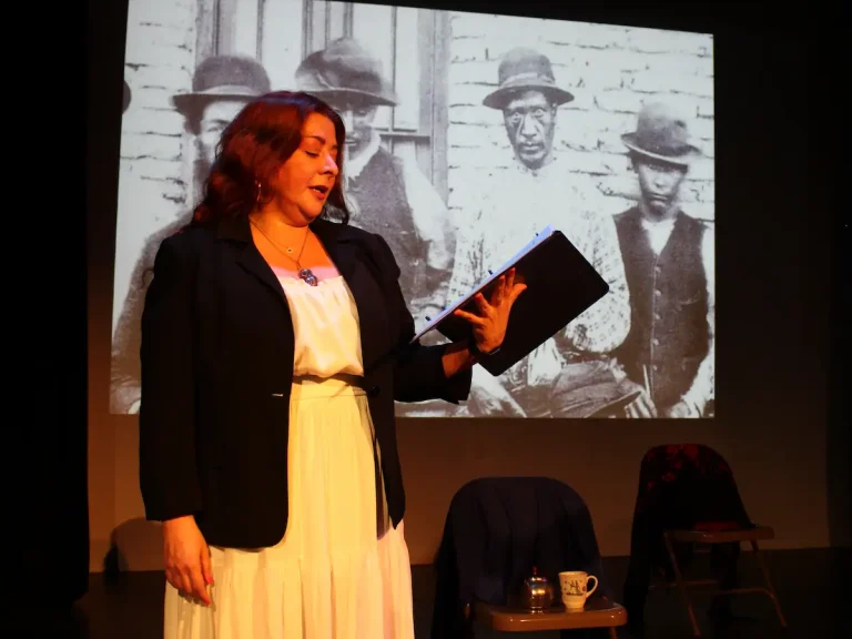 Vanessa Codorniu stands on stage reading with screen behind her.