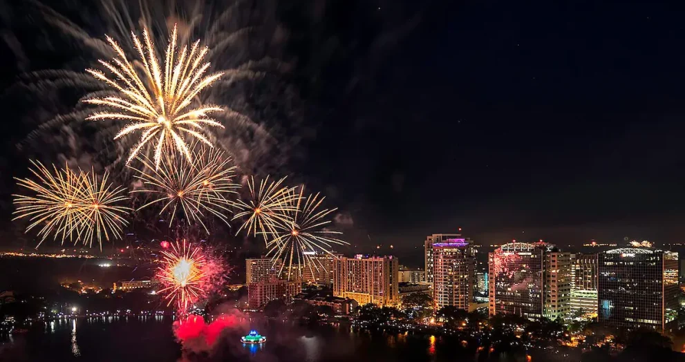 Fireworks over the Lake Eola Fountain with large buildings in the dark sky horizon line.