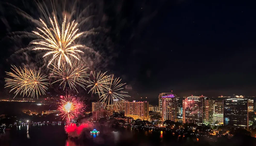 Fireworks over the Lake Eola Fountain with large buildings in the dark sky horizon line.
