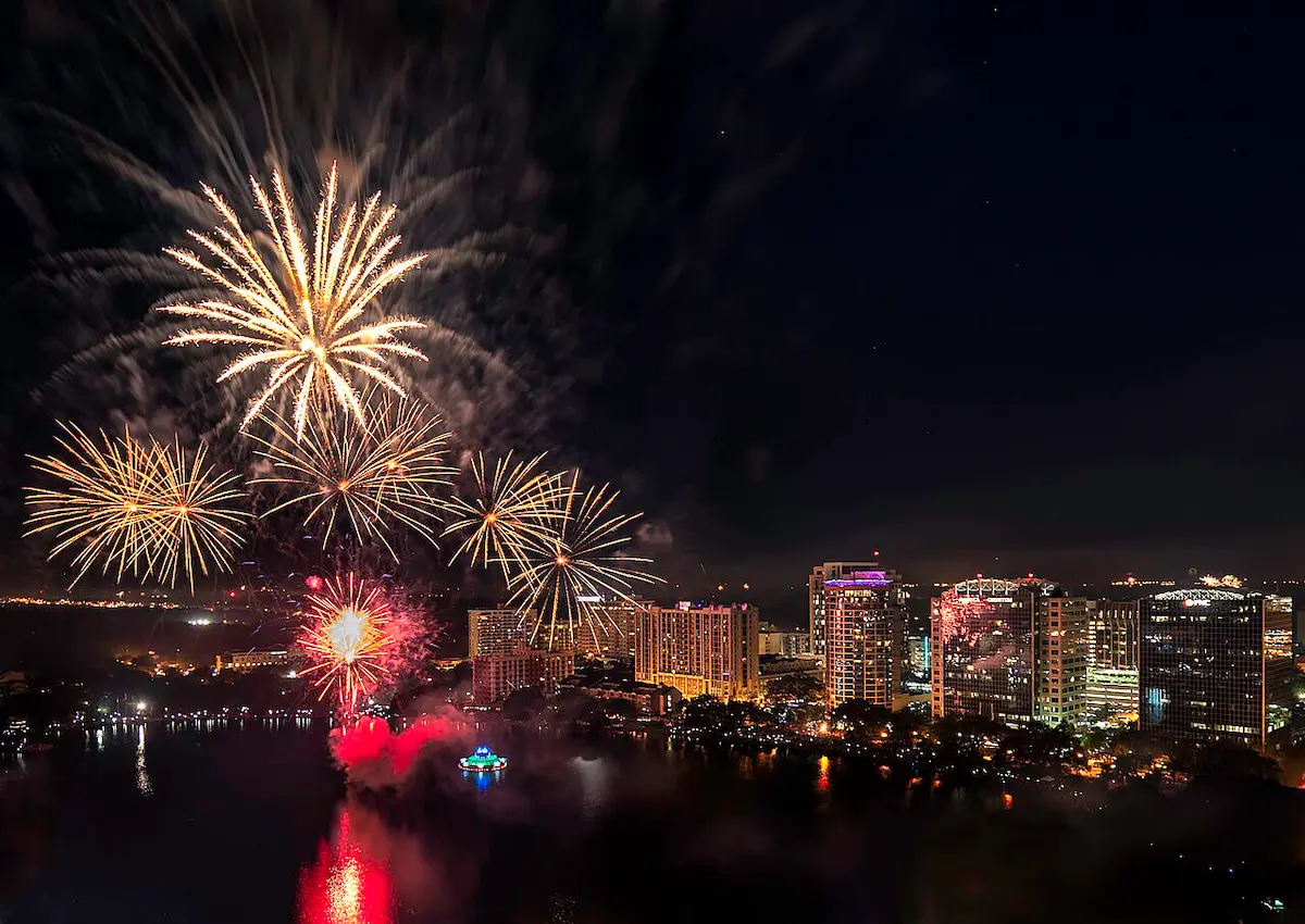 Fireworks over the Lake Eola Fountain with large buildings in the dark sky horizon line.