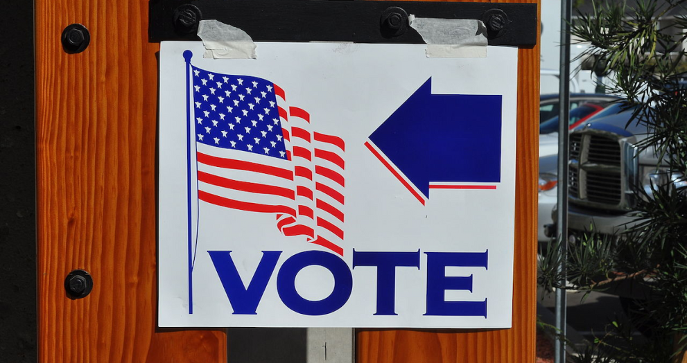 white sign has American (U.S.) flag and the word "vote" and an arrow in blue