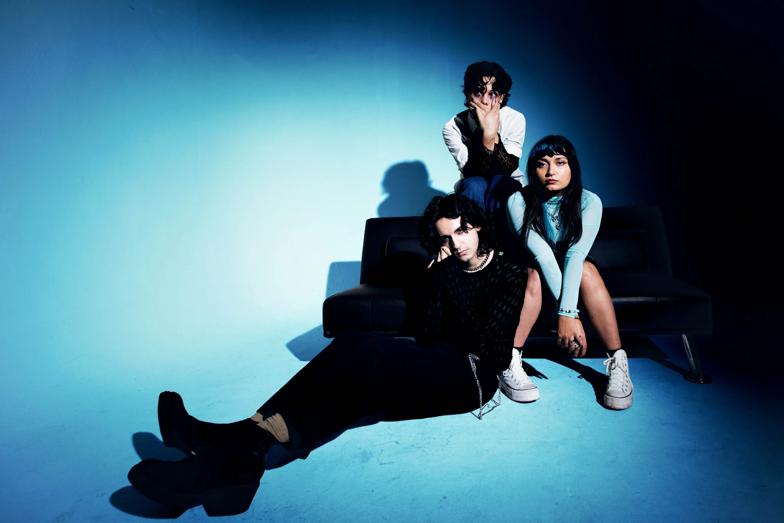 The three members of Orlando indie band Mirror Parts pose together sitting on the floor in a studio with blue high-contrast lighting.