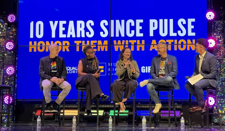 Five people sitting on stools on a stage participating in a panel discussion in front of a blue screen that reads "10 Years Since Pulse: Honor Them With Action."