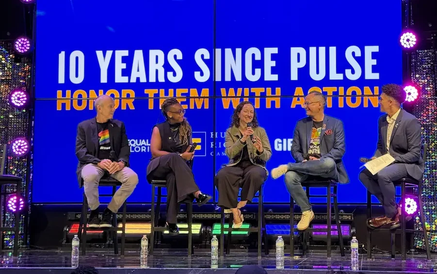 Five people sitting on stools on a stage participating in a panel discussion in front of a blue screen that reads "10 Years Since Pulse: Honor Them With Action."