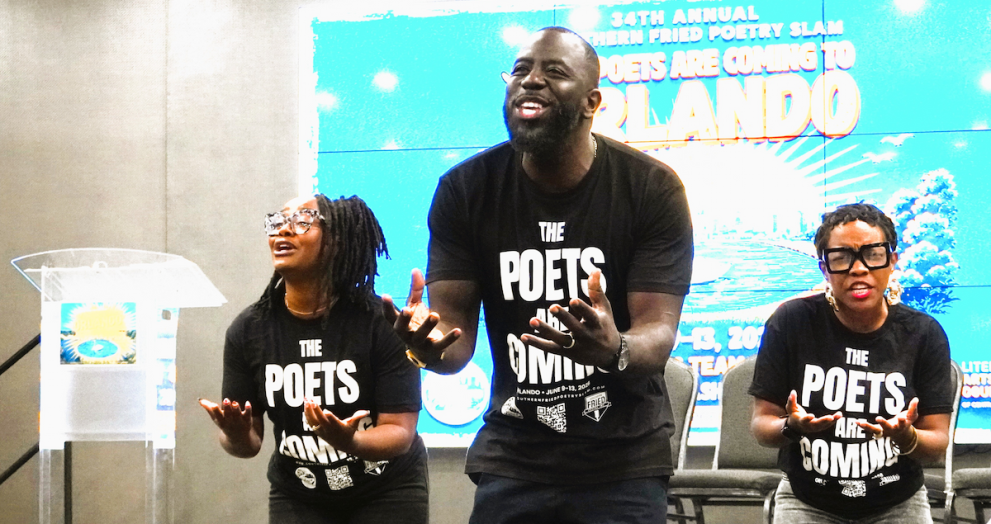 Three poets wearing matching black t-shirts that read "The Poets Are Coming" perform with expressive hand gestures on a stage in Orlando, Florida.