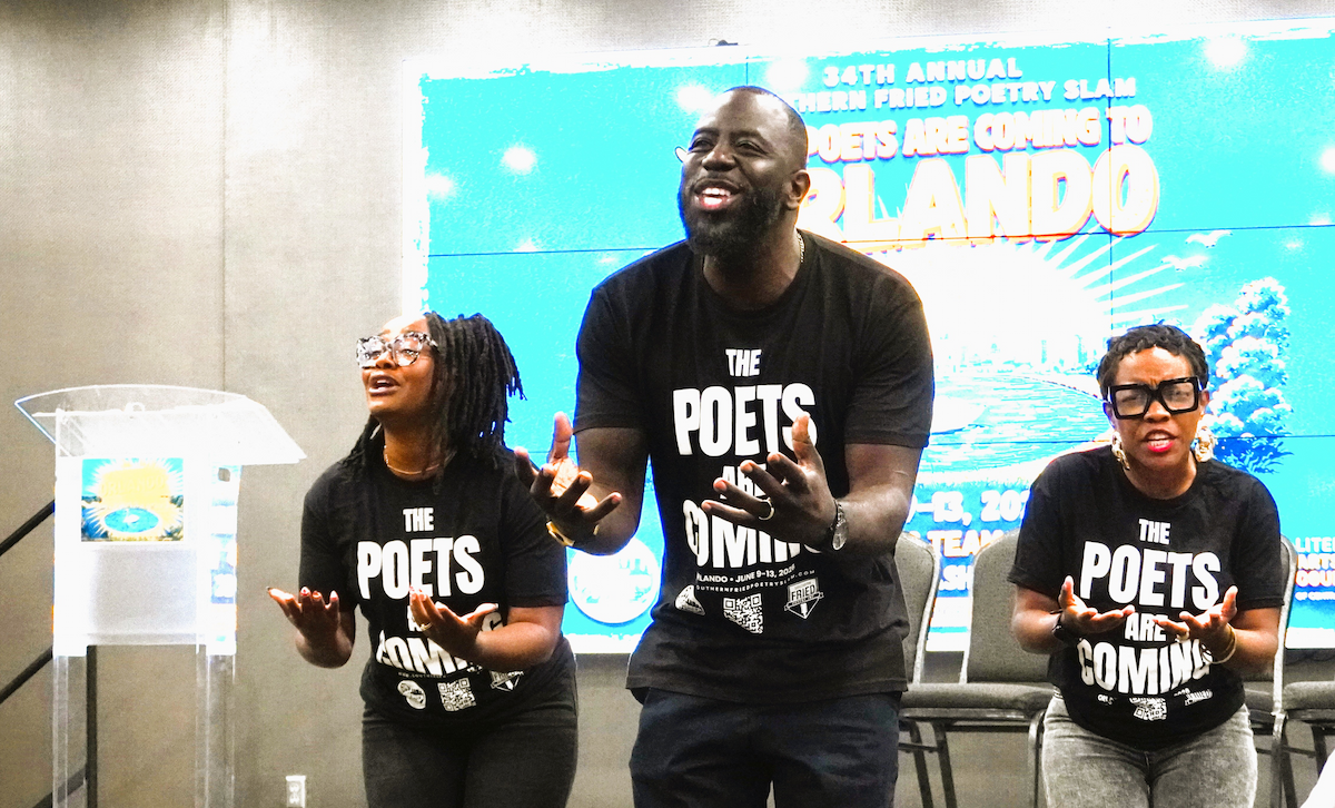Three poets wearing matching black t-shirts that read "The Poets Are Coming" perform with expressive hand gestures on a stage in Orlando, Florida.