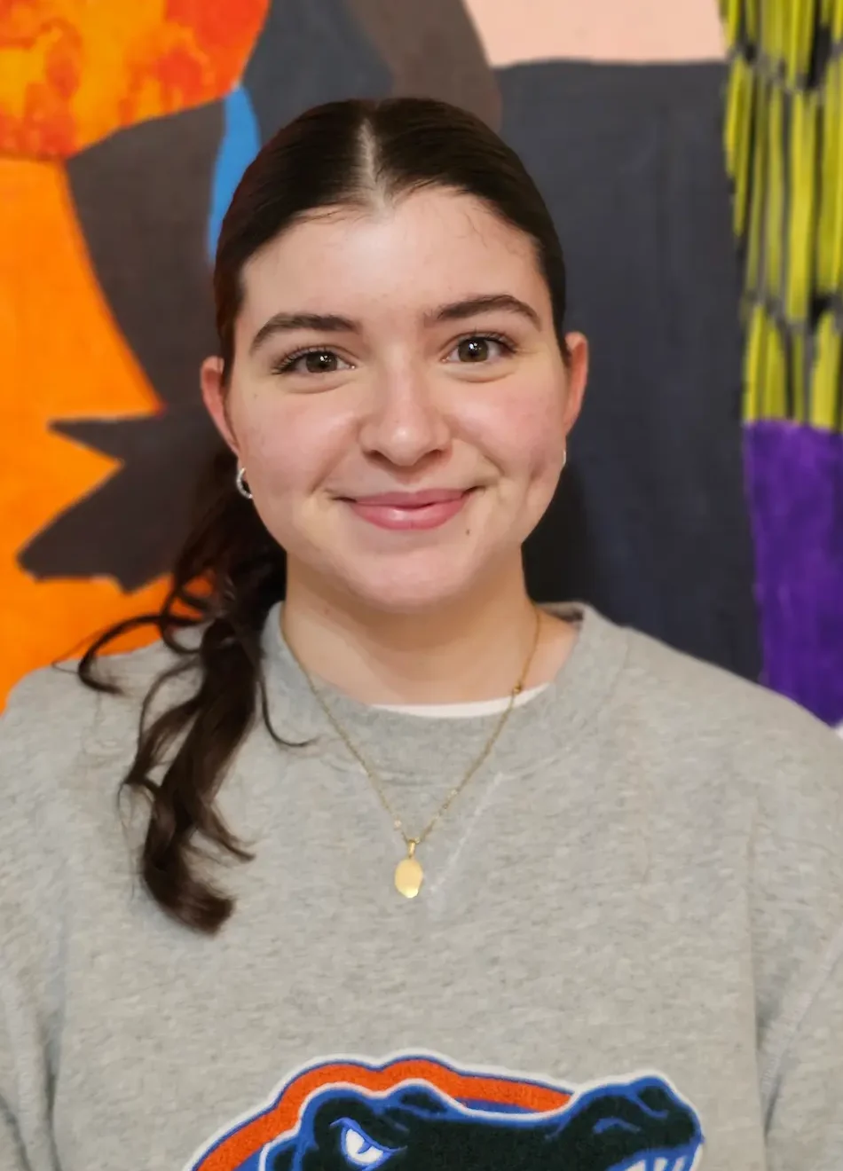 Daniella Tenorio wears a gray University of Florida sweatshirt featuring the Gators logo. She has dark brown hair pulled back into a ponytail and wears a gold necklace.