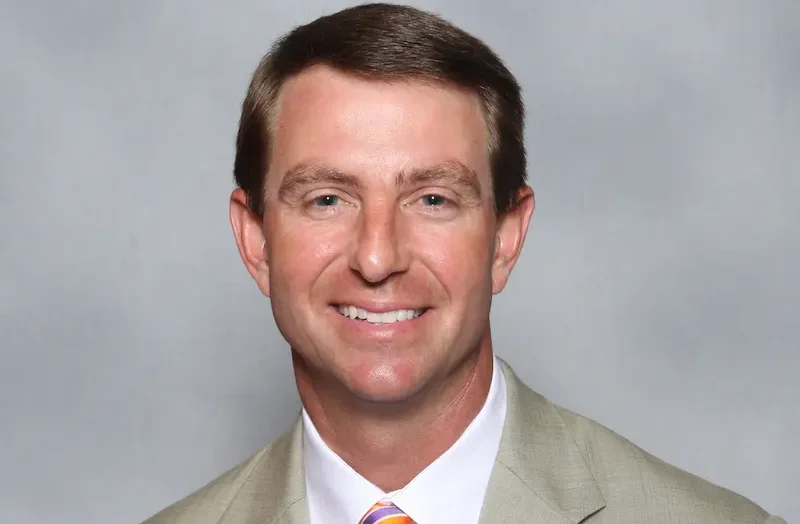 Dabo Swinney, Clemson college football coach, wearing a beige jacket and orange tie for official coaching staff photo
